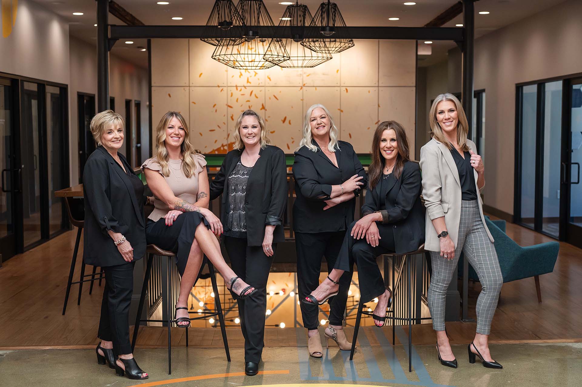 A group of six professional women from the ELTA Group posing confidently in a modern office space. They are dressed in business attire, showcasing a mix of blazers, dresses, and heels.